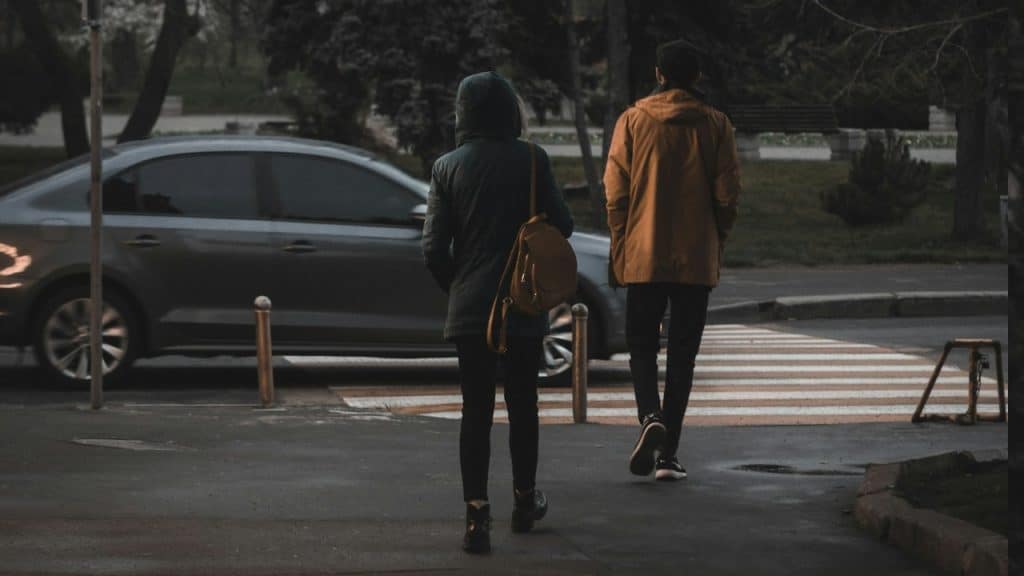 A man and a woman walking near a gray car.