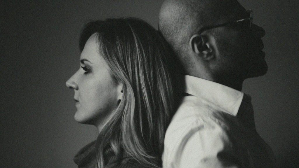 A black and white profile photo of a woman and man leaning back to back.