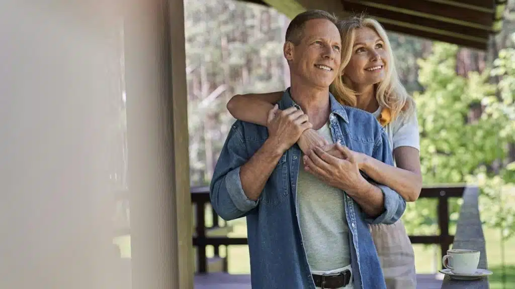 A woman hugging a man from behind while they are standing on the terrace.