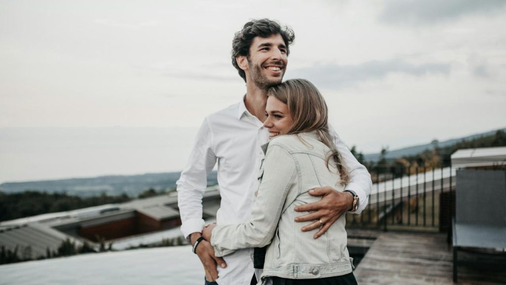 A couple smiling and hugging on top of a building.