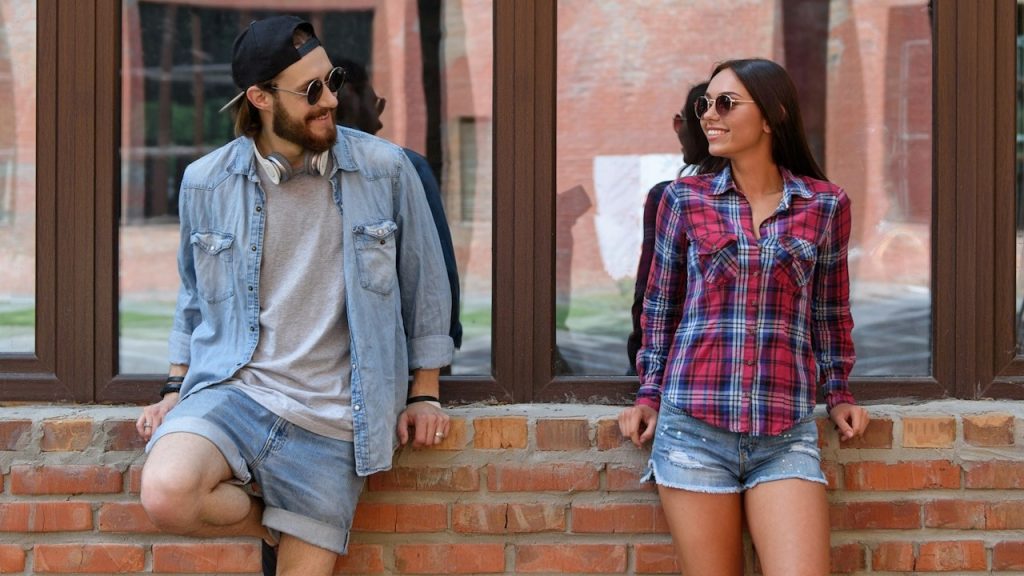 A joyful young man and woman are talking and flirting; they are looking at each other and smiling.