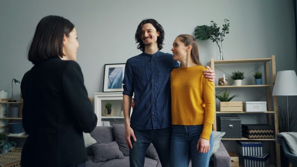 A couple smiling while standing close together in front of a smiling woman.