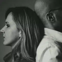 A black and white profile photo of a woman and man leaning back to back.