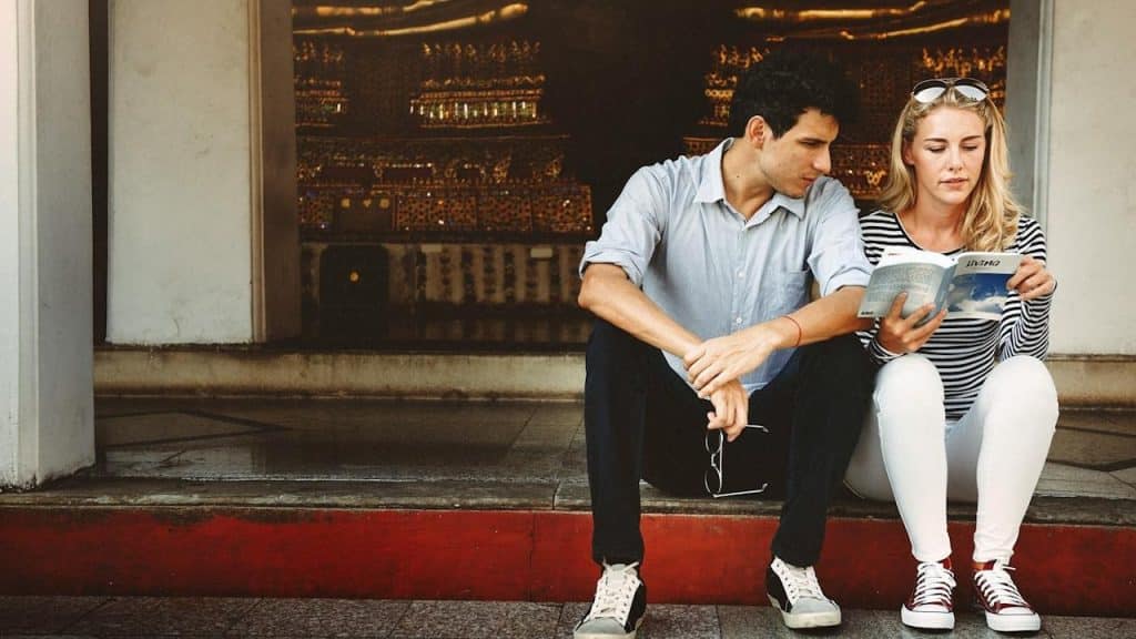 A couple sitting on stairs and reading a book.
