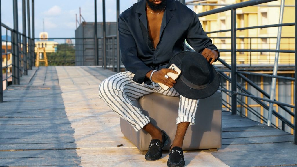 A man in a black jacket and black pants sitting on a gray wooden bench during the daytime.