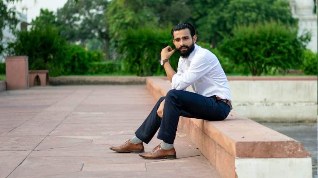 A man in a white dress shirt and blue jeans sitting on a bench