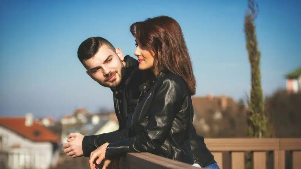 A man in a black leather jacket kissing a woman in a black leather jacket during daytime.