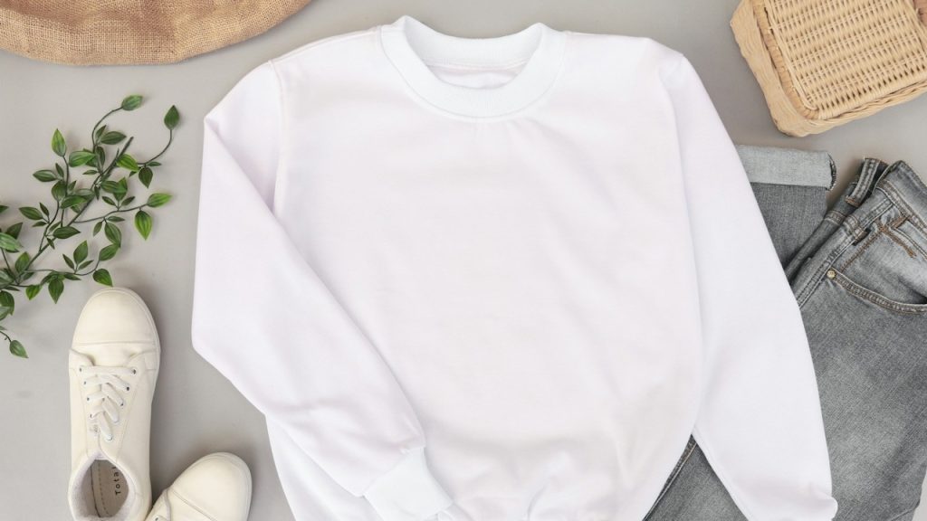 A knitted white sweater lying next to white sneakers.