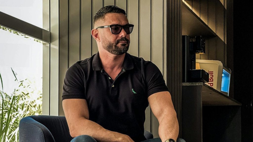 A man wearing a black T-shirt and sunglasses in a living room.