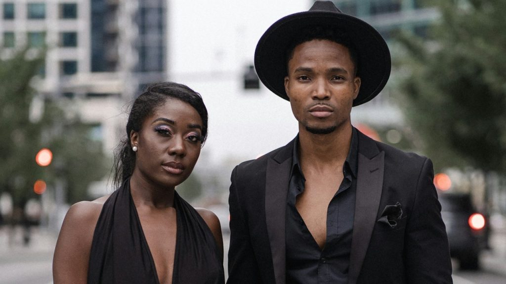 A woman in a black dress and black blazer standing beside a woman in a black dress.