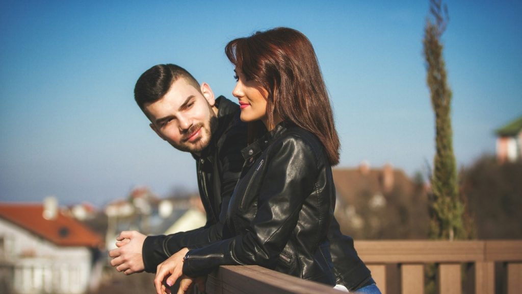 A man in a black leather jacket kissing a woman in a black leather jacket during daytime