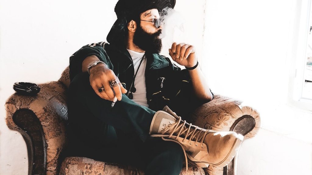 A man wearing black hat and leather boots is sitting on a sofa.