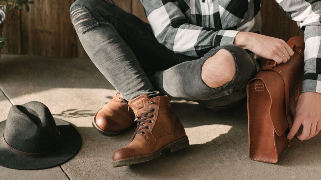A person holding a brown-leather briefcase and wearing brown-leather boots is sitting on the floor.