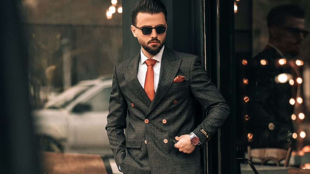 A man in a suit leaning against a brick wall.