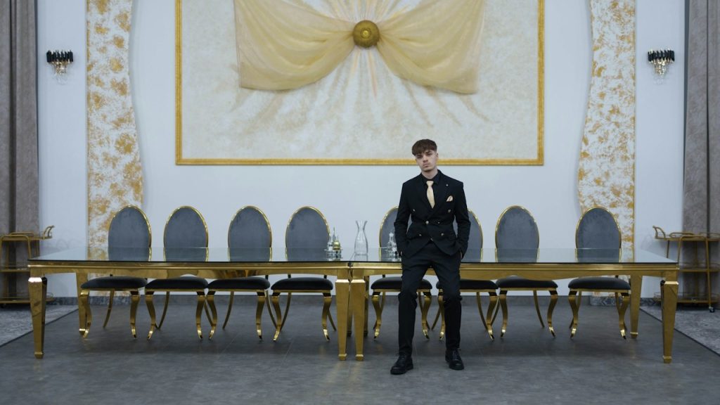 A man in a suit standing in a grand hall with a long table.
