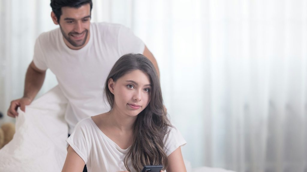 A man looking at his wife using a phone while standing behind her.