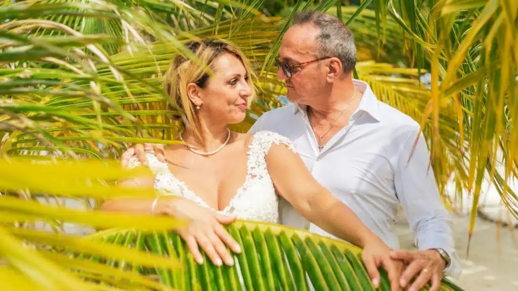A man and woman standing next to each other under palm trees.