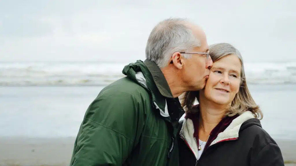 A man kissing a woman on the cheek beside a body of water.