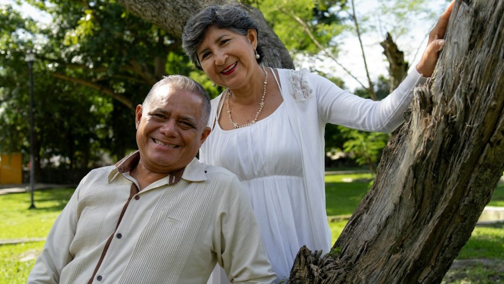 A smiling couple poses near a tree outdoors.