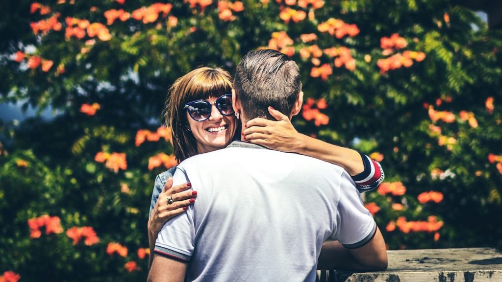A man and woman hugging in front of a floral tree.
