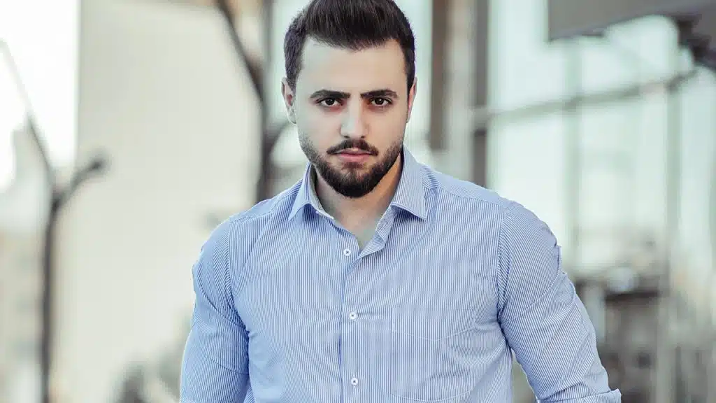 A man in a blue dress shirt and black dress pants standing.