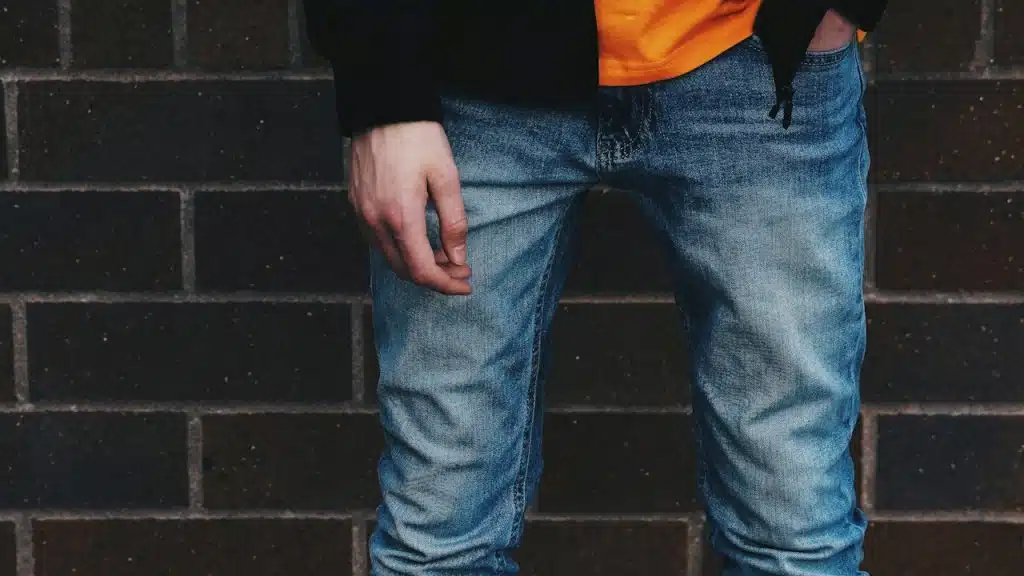 A man standing while wearing skinny jeans with a wall in the background.