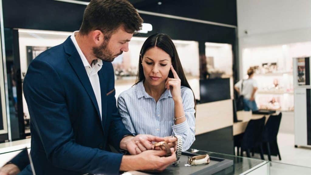 A man in a suit and a woman look closely at watches in a jewelry store.