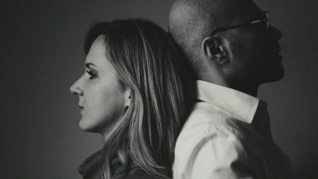 A black and white profile photo of a woman and man leaning back to back.