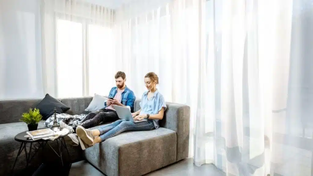 A couple sitting on a couch, both focusing on screens during a conversation