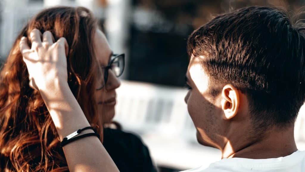 A man in a white shirt and a woman wearing black sunglasses are sitting together outdoors.