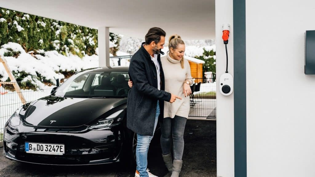 A couple standing by their electric car next to a charger.