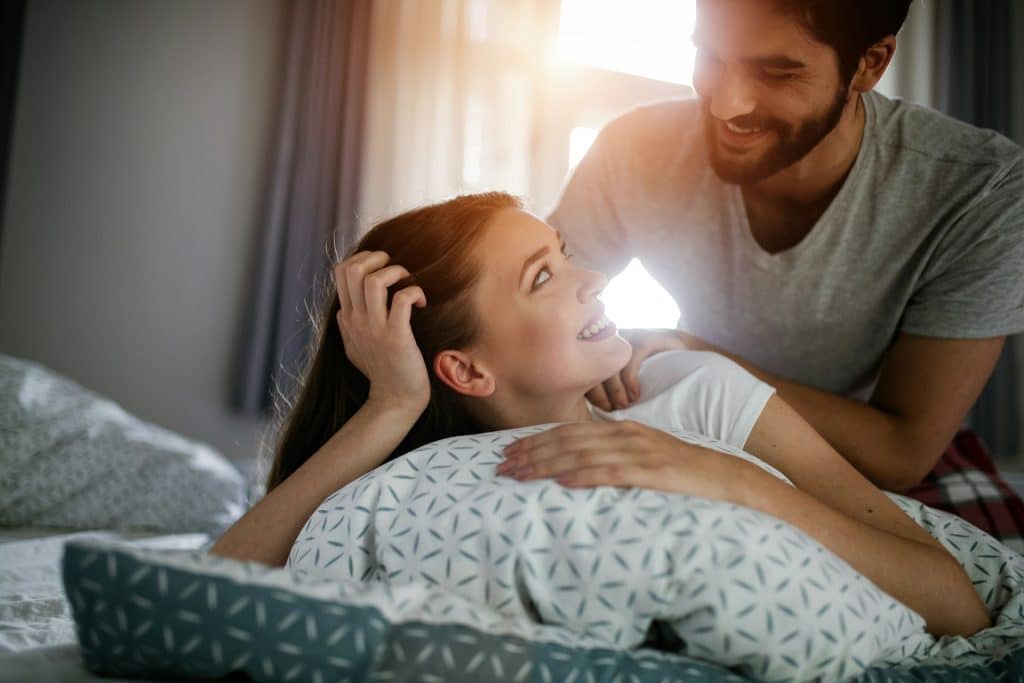 A boyfriend is giving a massage for his beautiful girlfriend relaxing in a bed.