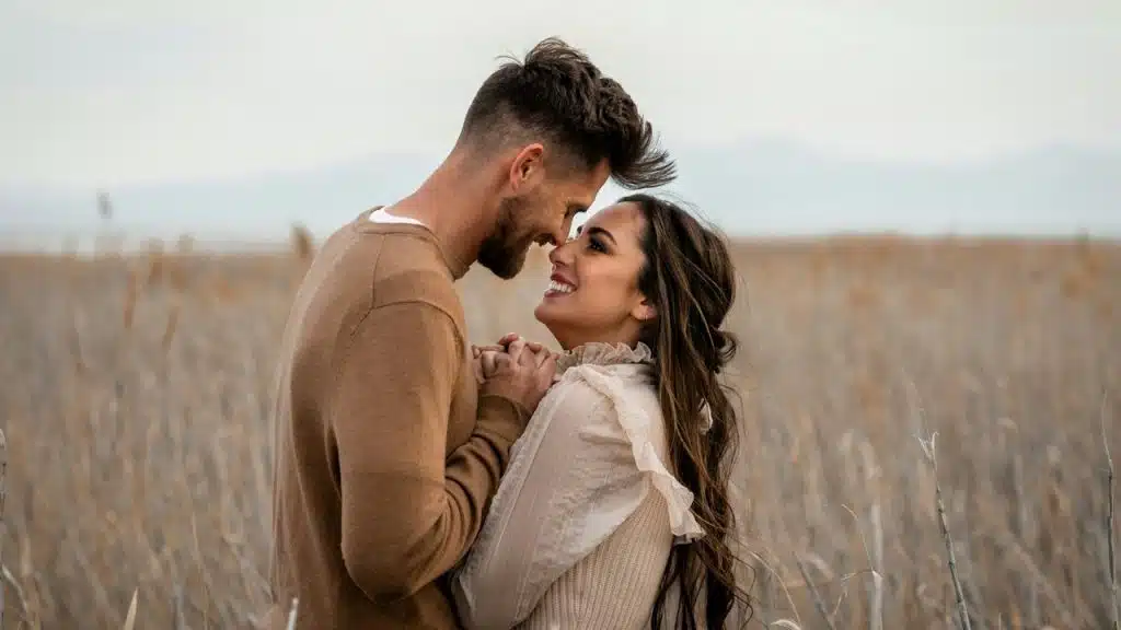 Couple looks at each other lovingly in a field.