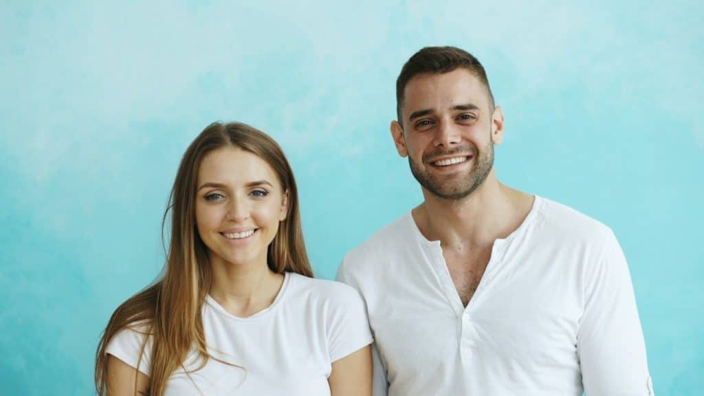 A smiling couple in white shirts against a blue background.