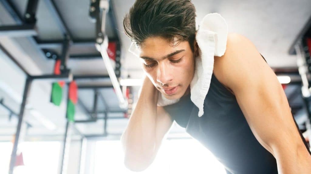 A tired man with a towel around his neck resting after a workout.