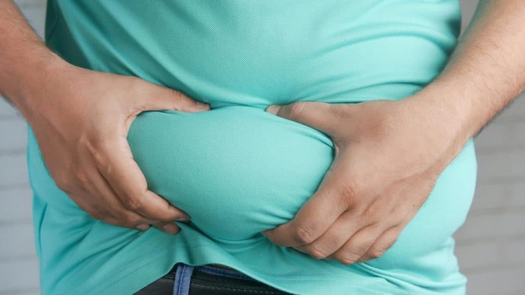 A person grabbing belly fat through a shirt.