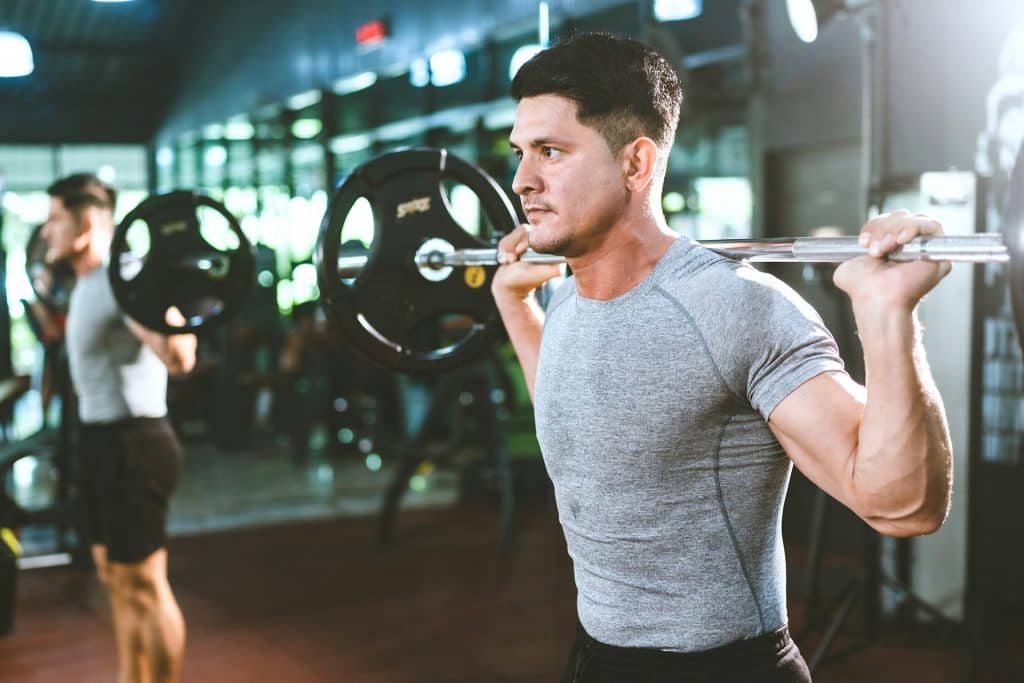 A man with a barbell placed on his upper back.