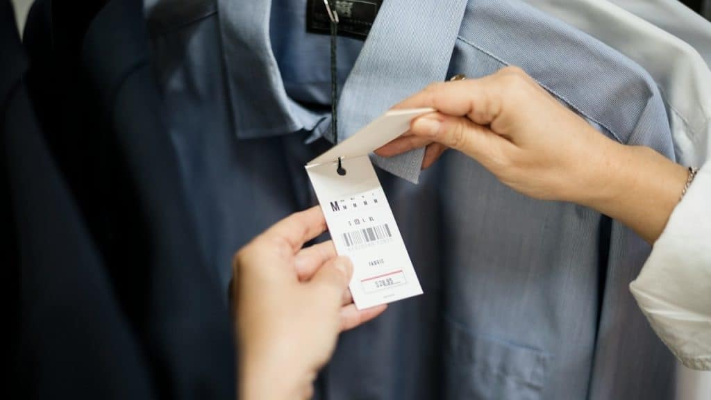 A person's hands holding and inspecting the price tag of a shirt.