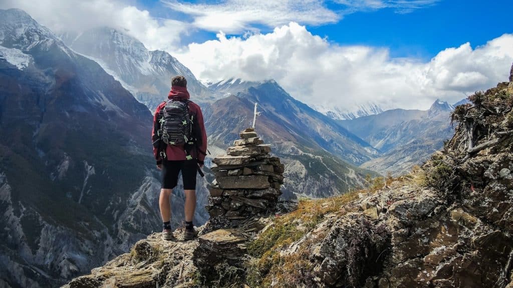 A hiker with a backpack standing on a rocky mountain peak.