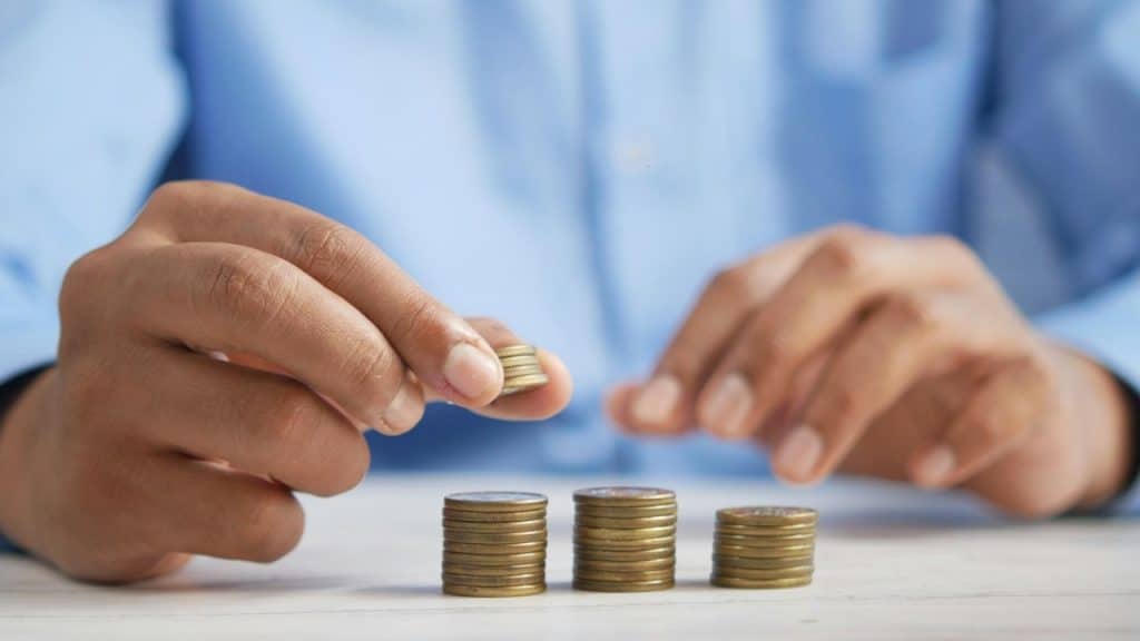 A close-up of a person's hands stacking gold coins into three neat piles.