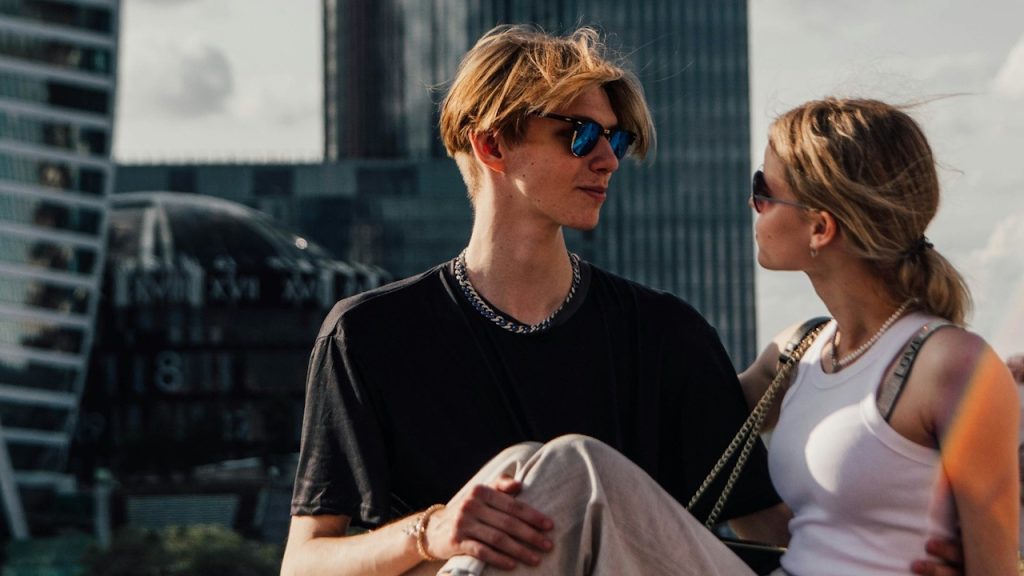 A man and a woman sitting on a ledge in front of a cityscape.