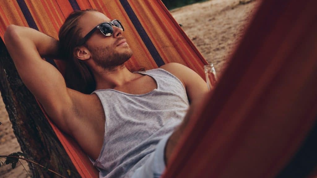 A man with long hair and sunglasses relaxing in a hammock.