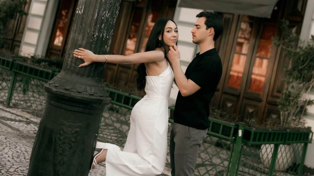 A couple posing outdoors, with the woman leaning against a lamppost and the man gently touching her chin.
