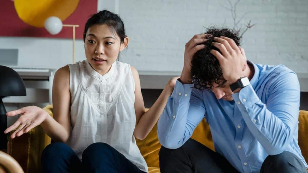 A woman gestures while speaking to a man who has his hands on his head in distress.