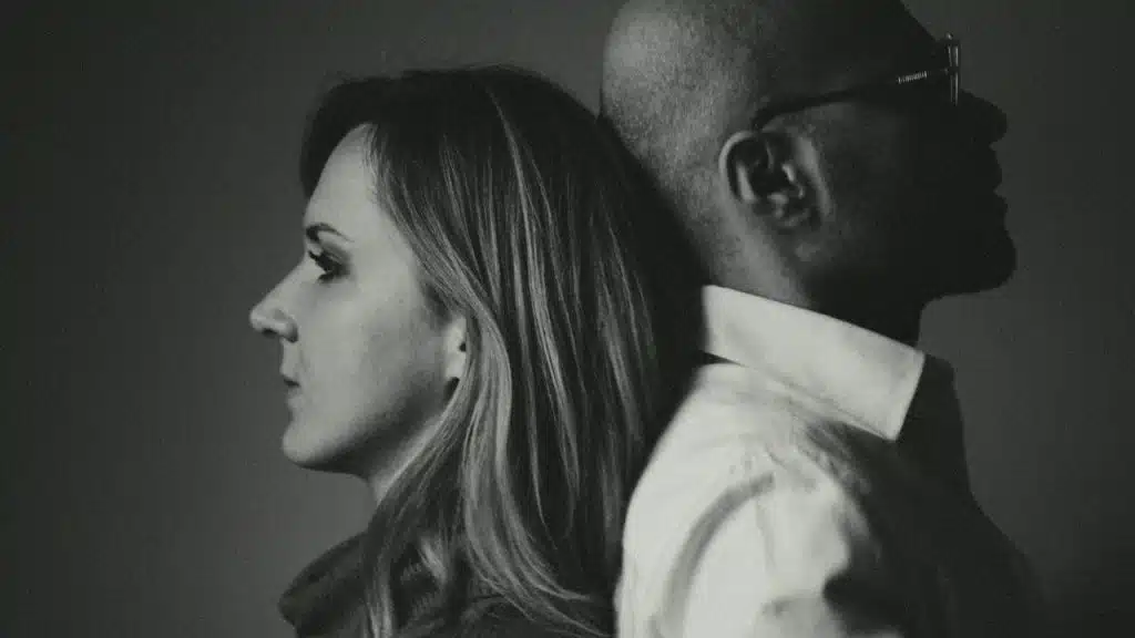 A black and white profile photo of a woman and man leaning back to back.