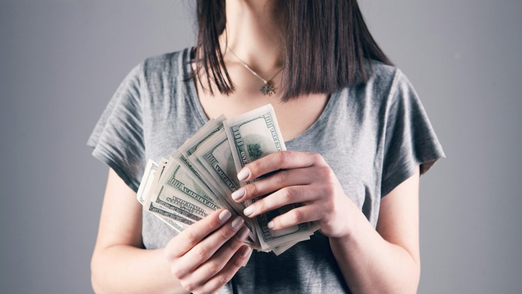 A woman holding several hundred dollar bills.