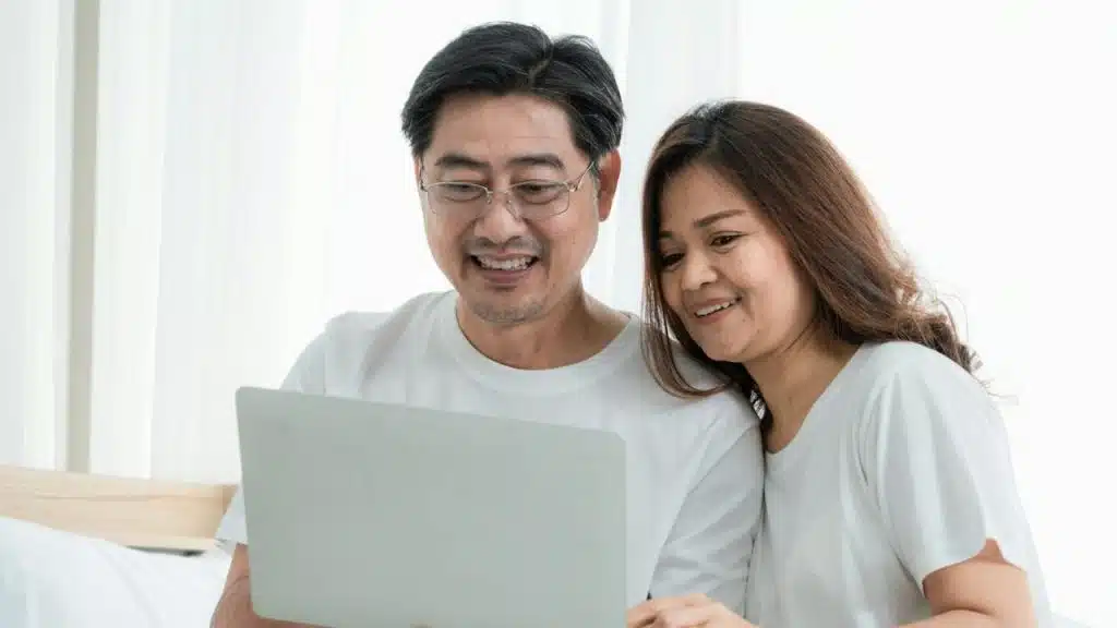 A mature Asian couple looking at a laptop and smiling.
