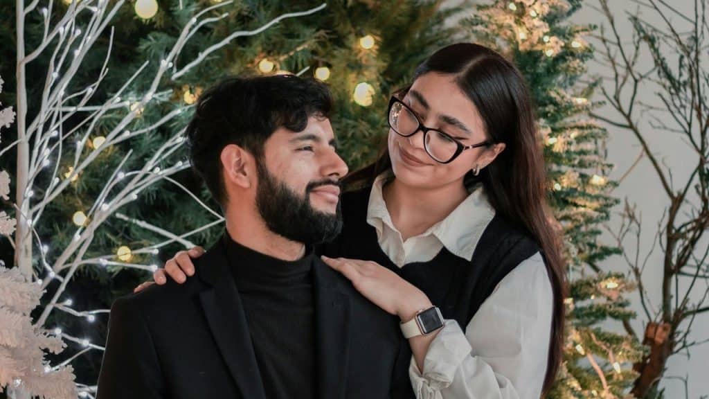 A couple posing for a picture in front of a Christmas tree.