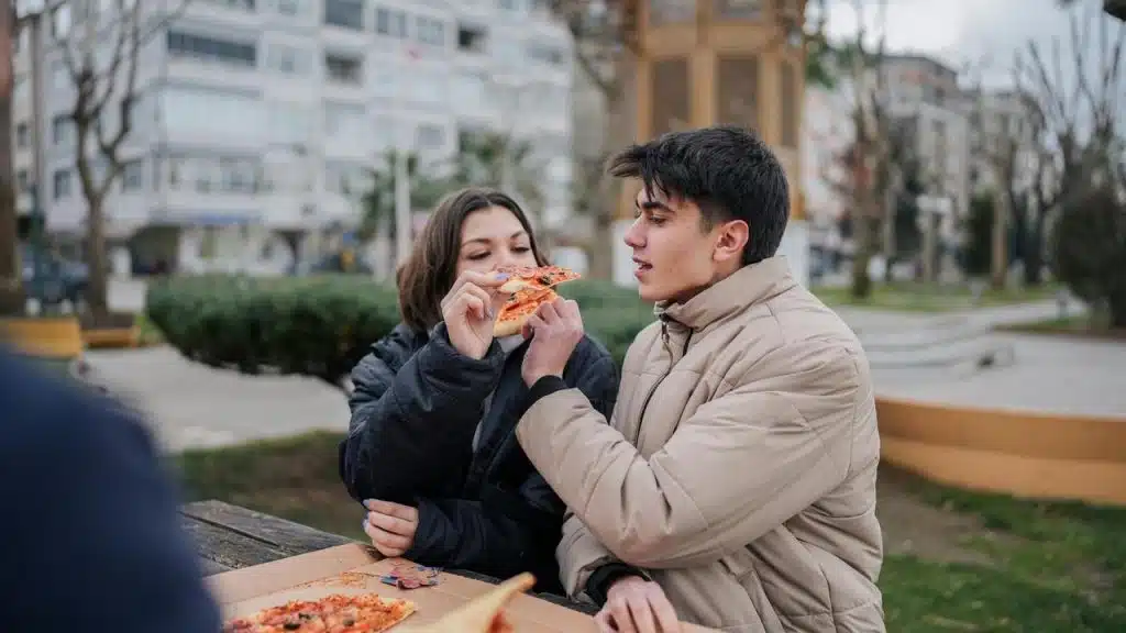 A couple sharing pizza at an outdoor park table.