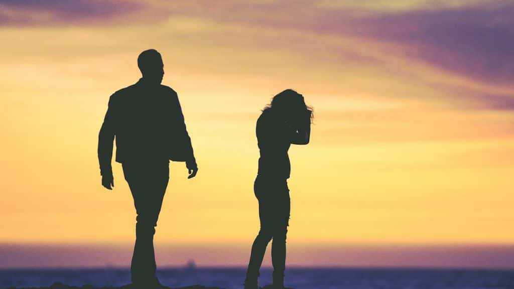 A silhouette of a couple at sunset while the woman looks frustrated.